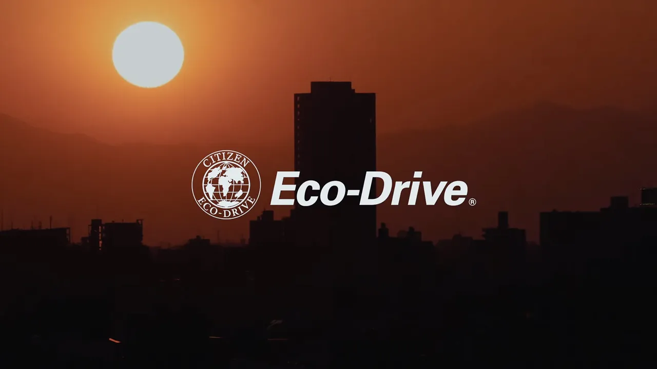 Citizen Eco-Drive Logo vor einer Silhouette einer Stadt bei Sonnenuntergang mit einer großen, hellen Sonne.